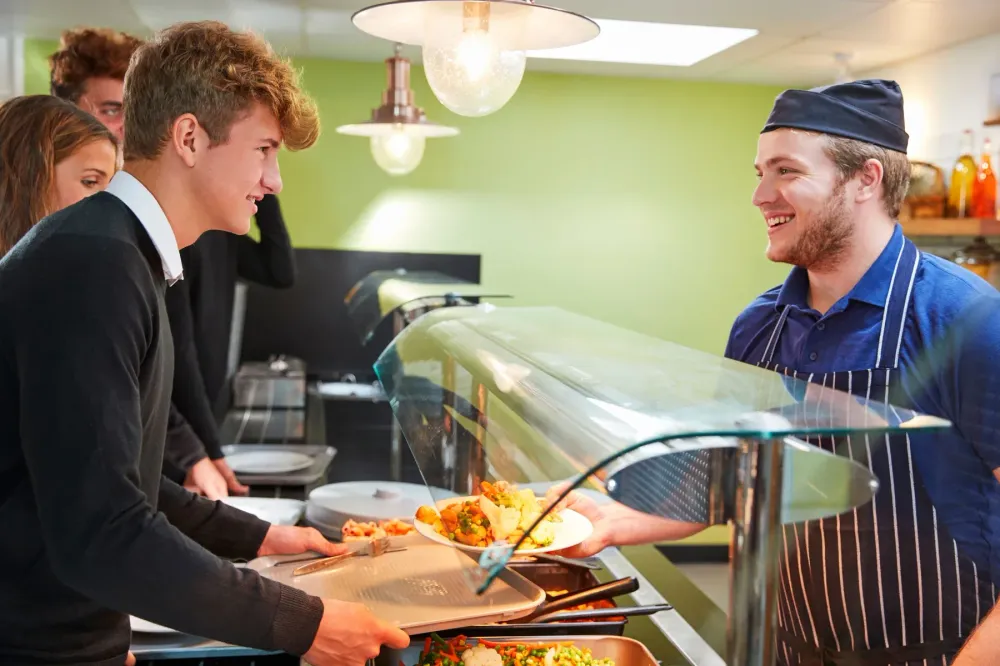Students being served at a cafeteria food line.