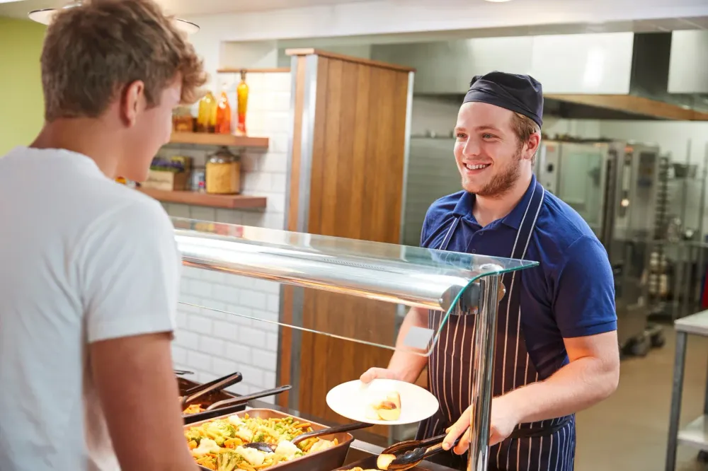 A student being served food by a smiling dining hall worker.