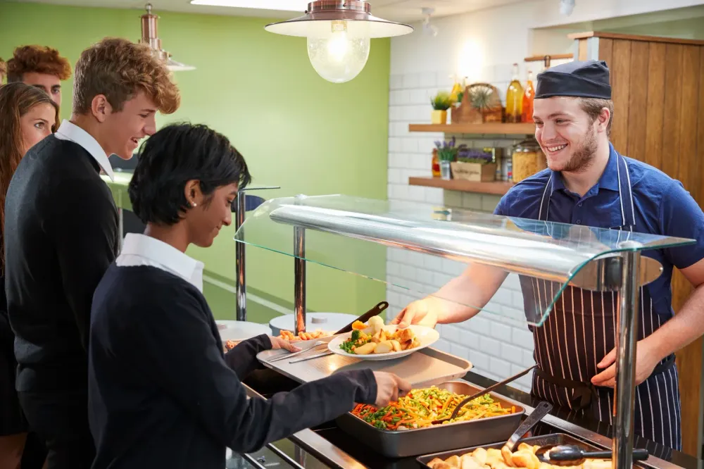 Students being served lunch at a school cafeteria serving line.