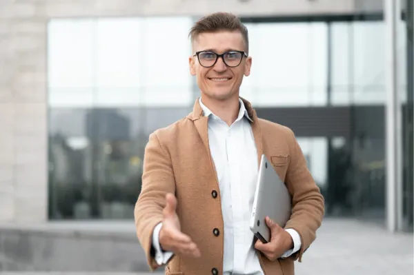 A smiling Touchwork team member holding a laptop and reaching out to shake hands.