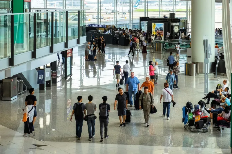 Travelers with luggage walking through a busy airport terminal concourse.