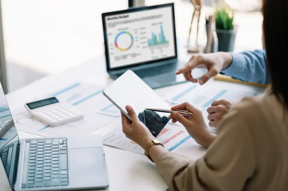 Two people reviewing charts and a dashboard at a desk.