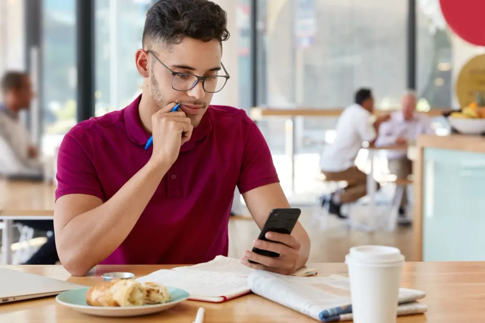 A man at a café table reading something on his phone.