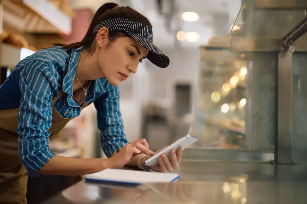 A food service worker checking a tablet at a serving counter.