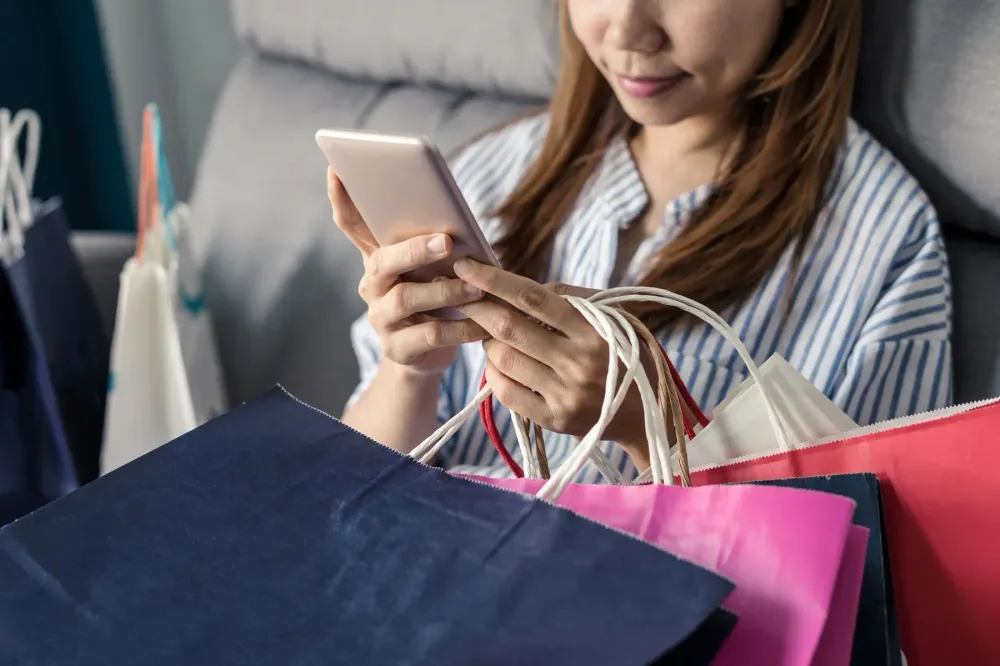 A shopper holding shopping bags while using her phone.